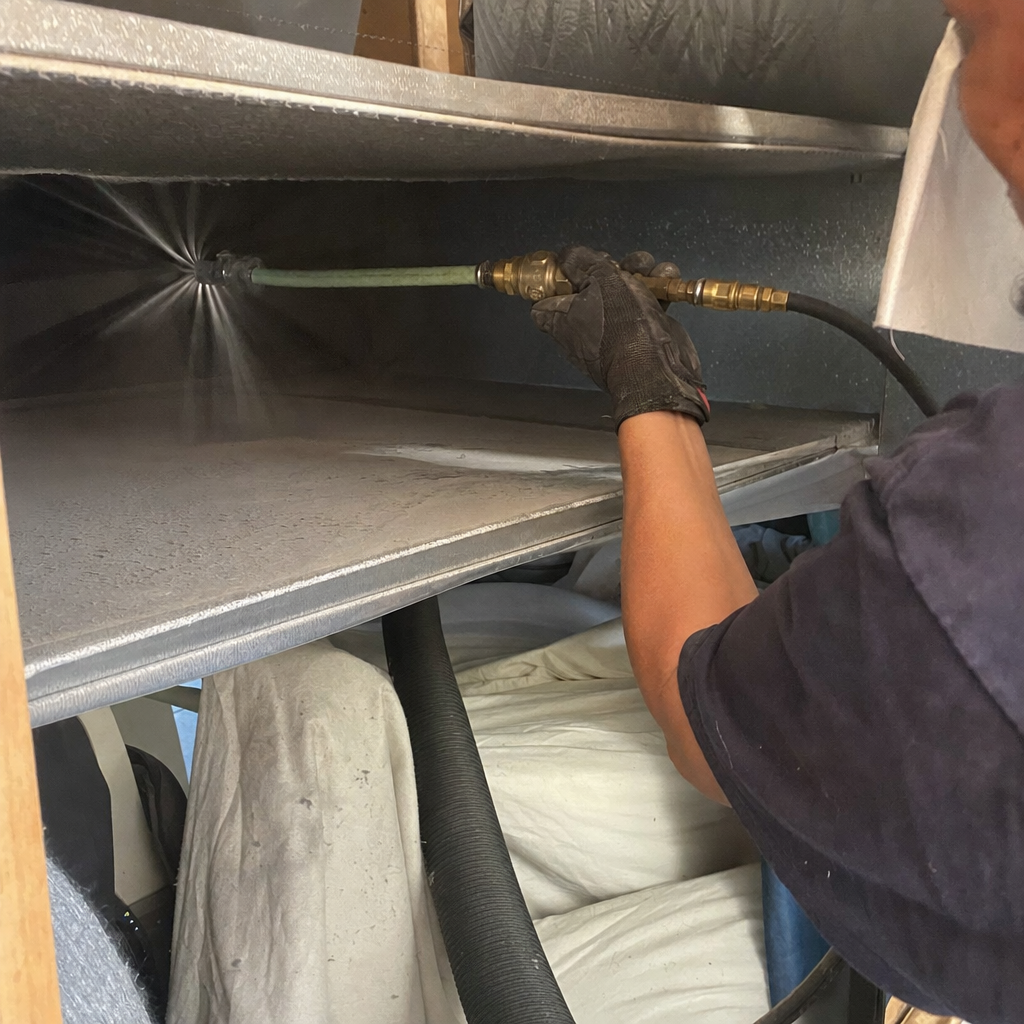 Professional air duct cleaning with spray nozzle inside metal ductwork.